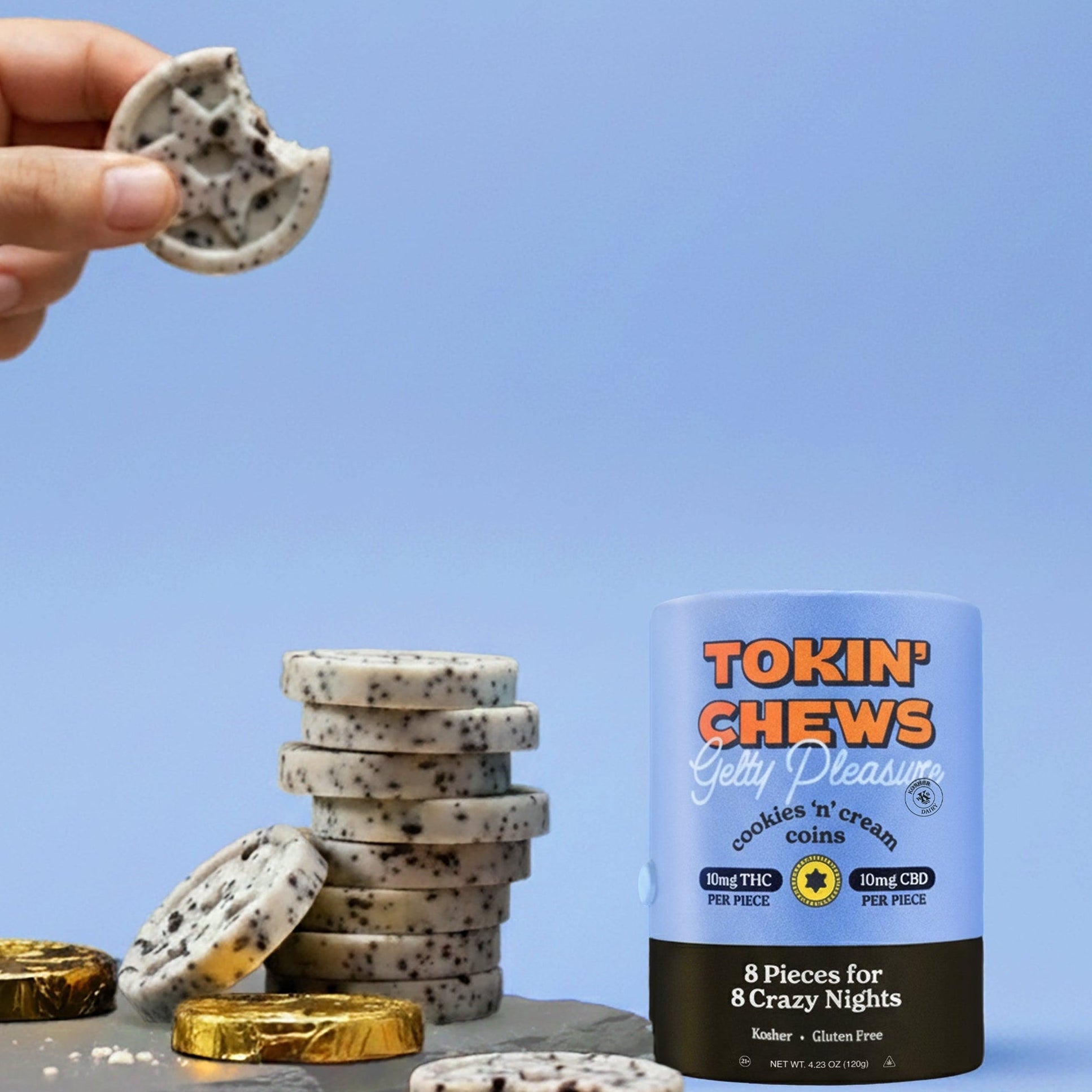 Hand holding gelt next to a container of cookies and creme gelt on a blue background